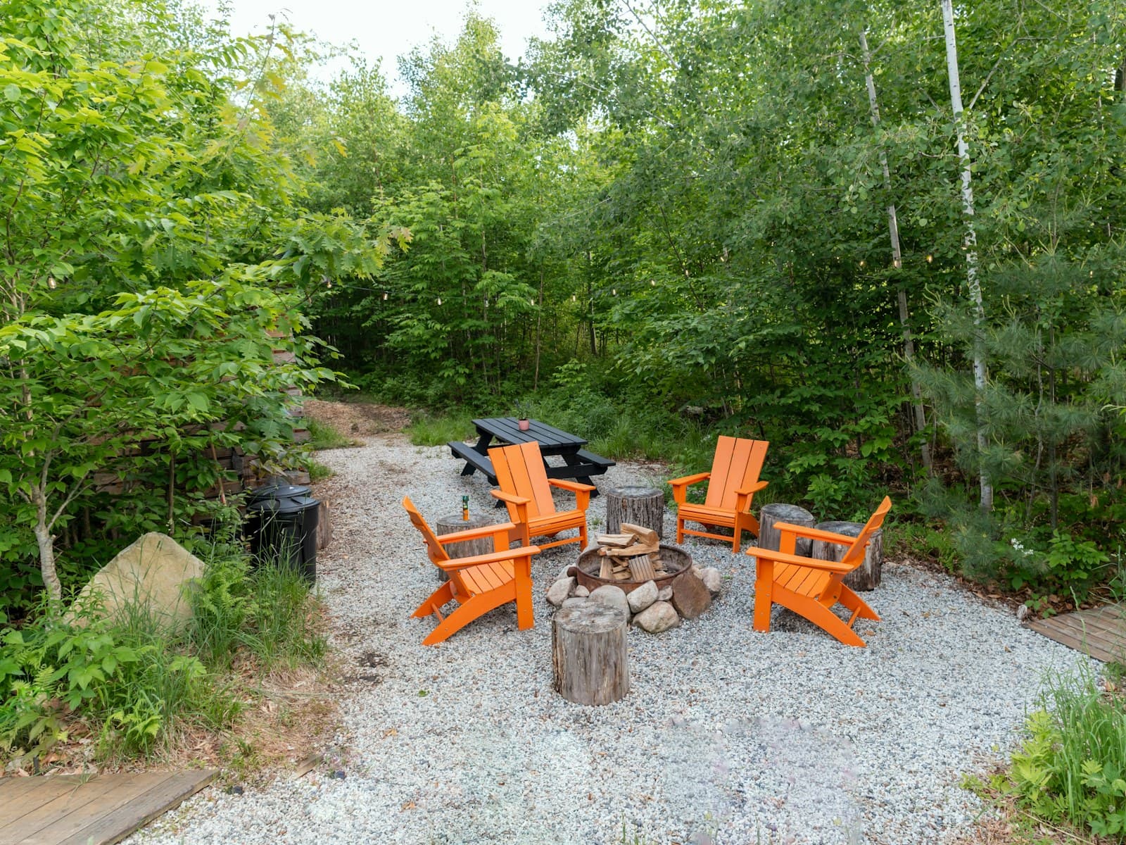 An outdoor fire pit ringed by orange chairs and a picnic table