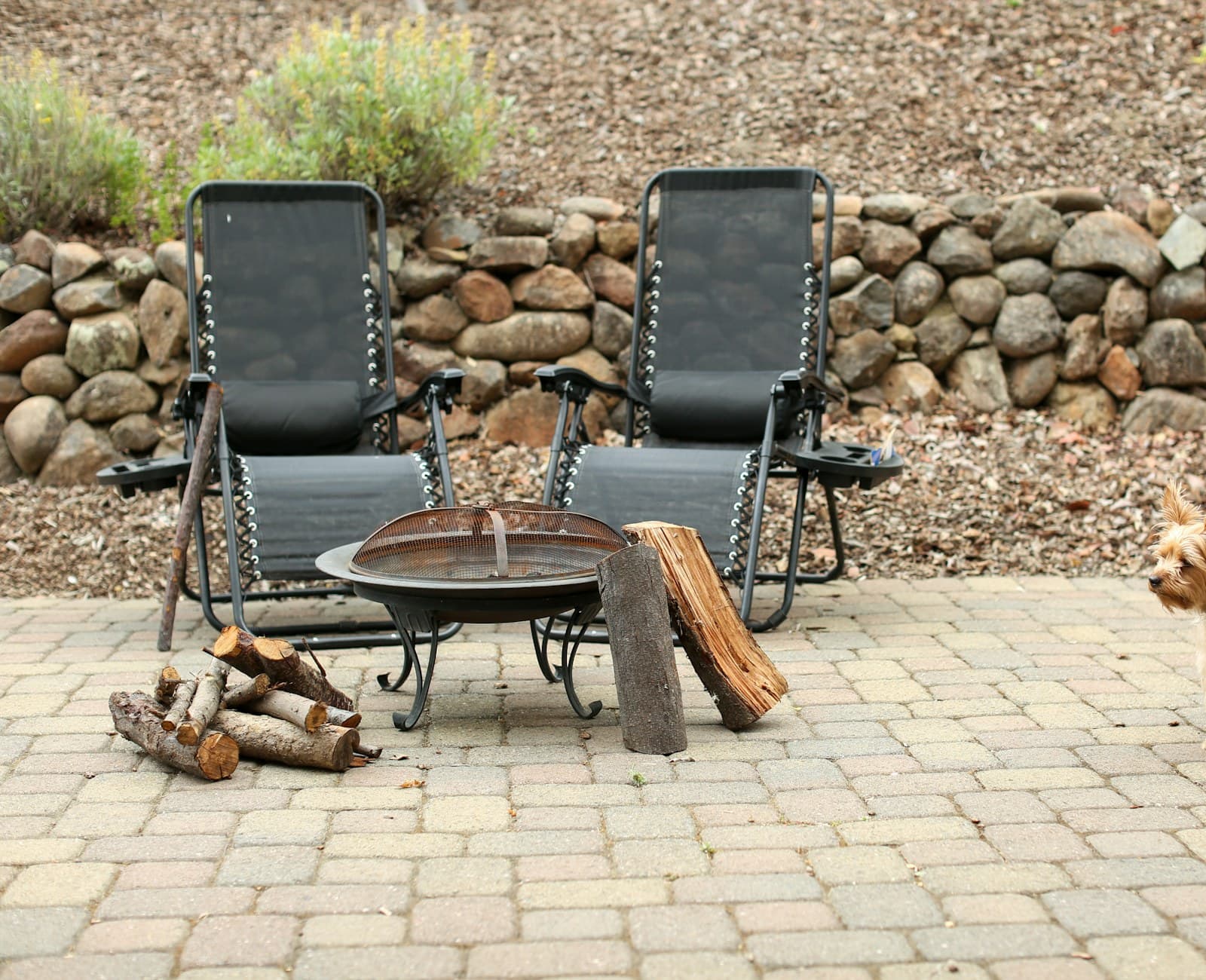Two chairs drawn up to a fire pit on a brick patio