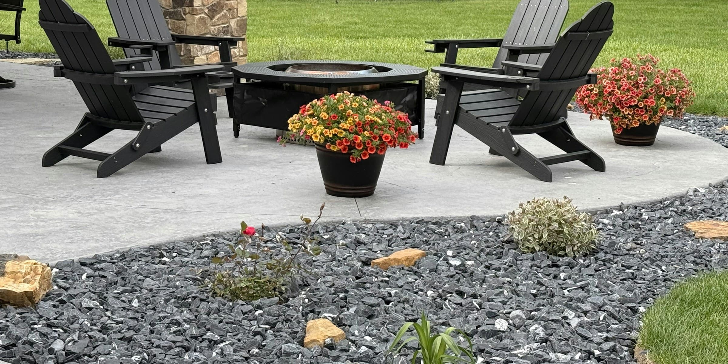 The finished backyard: a paved patio with Adirondack chairs, a fire pit and flowering borders
